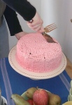 A pink cake is being cut into pieces